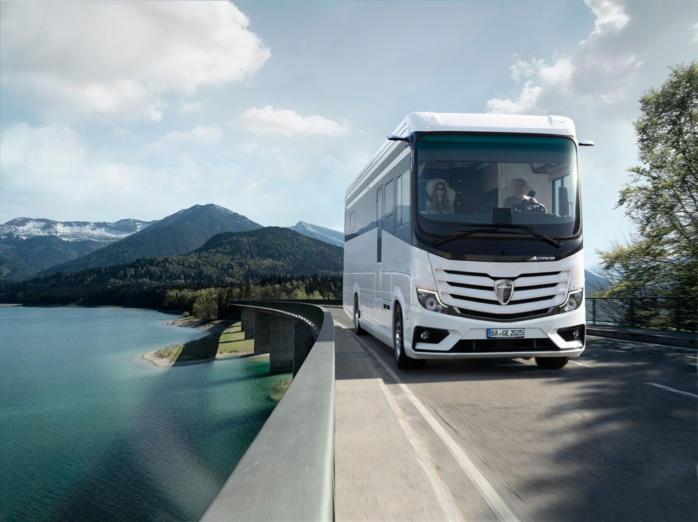Ein weißer moderner Reisebus fährt lächelndes Paar durch grüne Berglandschaft