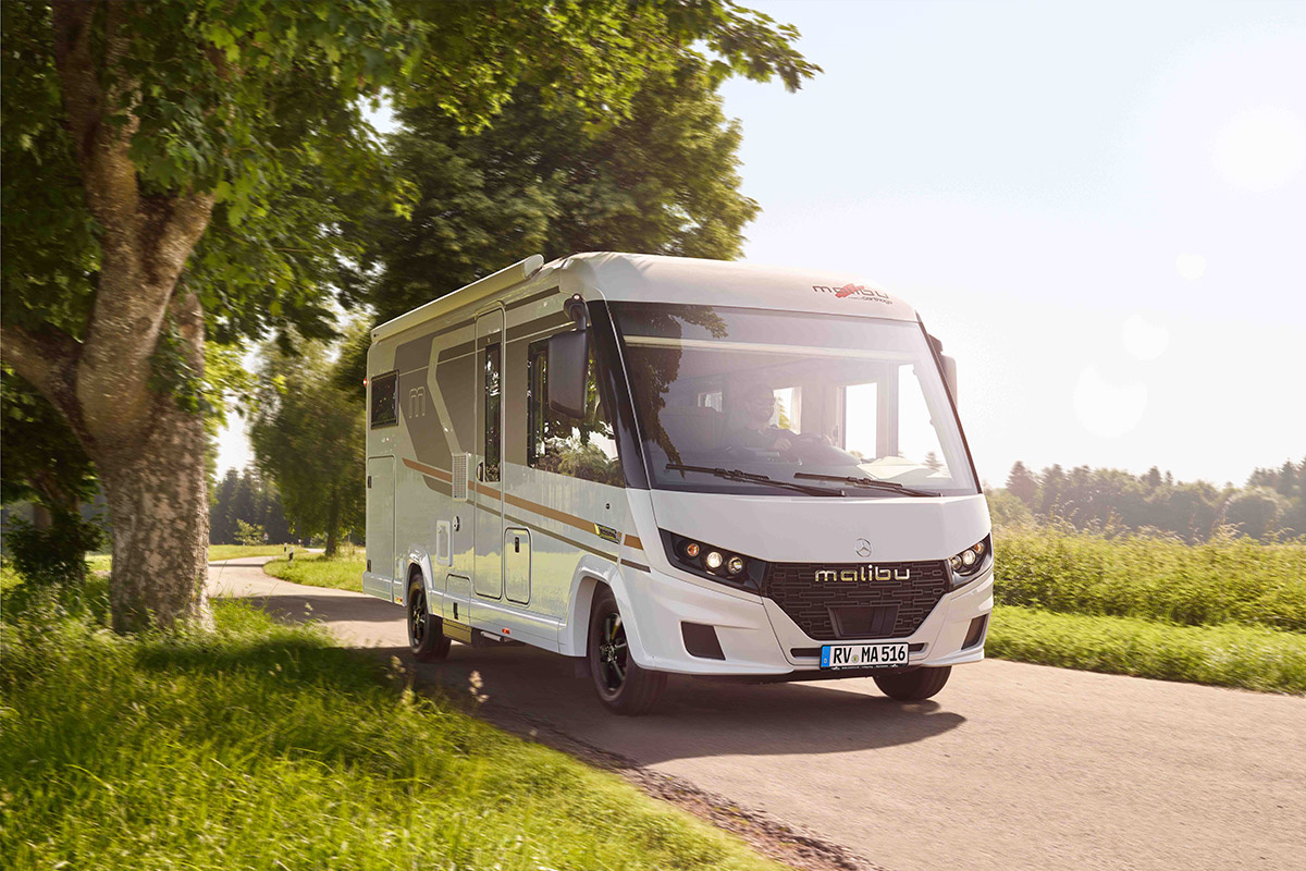 Ein weißes Wohnmobil fährt über eine sonnige Landstraße mit grüner Umgebung