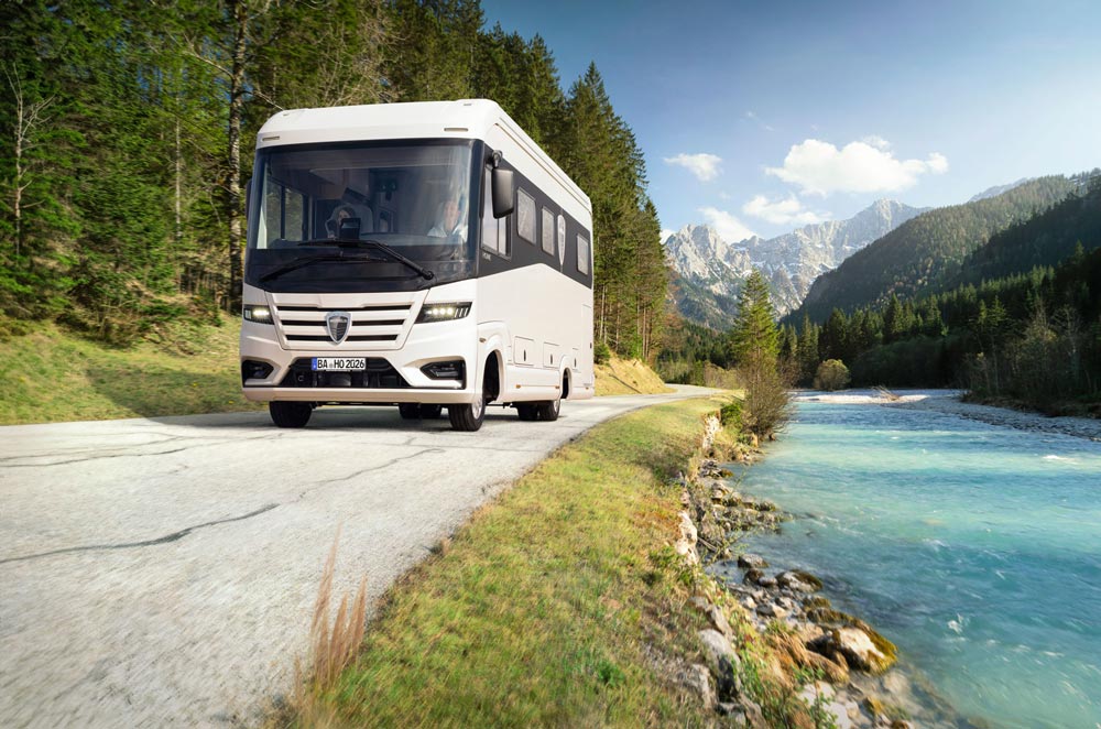 Ein weißer Reisebus fährt auf einer Landstraße am klaren Fluss mit Bergen entlang