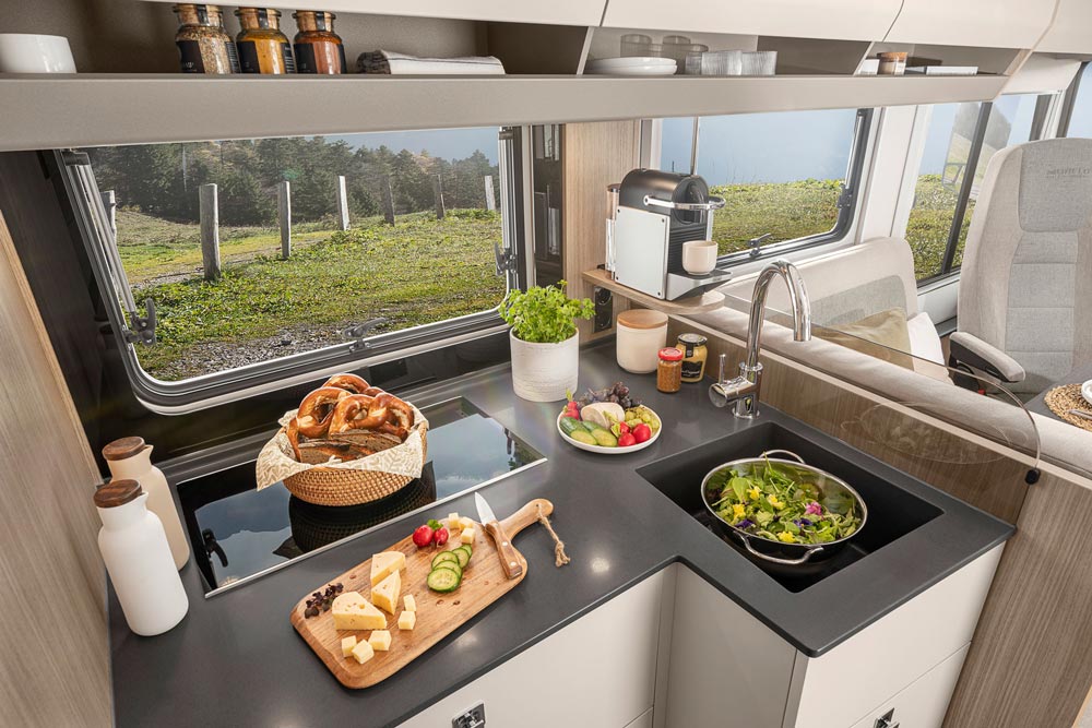 Moderne Wohnmobilküche mit frischem Gemüse Salat und Kräutern vor großem Fenster