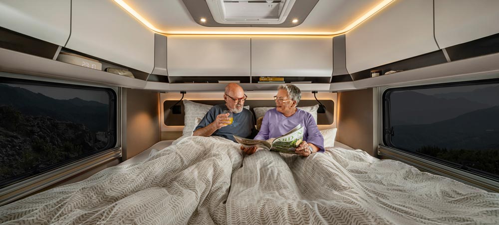 Zwei ältere Männer sitzen entspannt im Wohnmobilbett und unterhalten sich freundlich