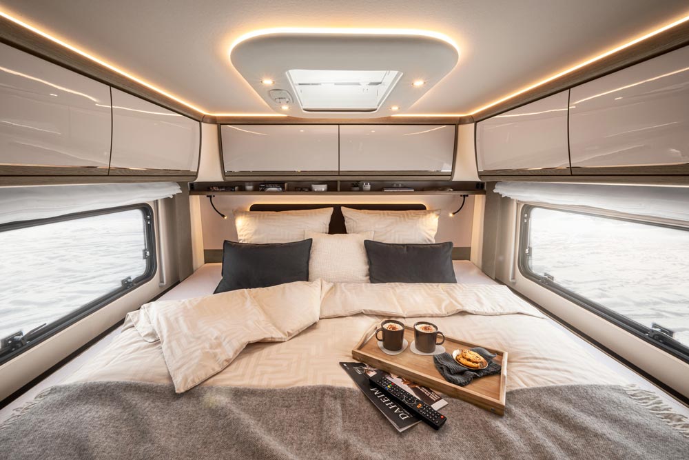 Gemütliches Wohnmobil Schlafzimmer mit hellen Kissen, grauen Decken und Frühstückstablett