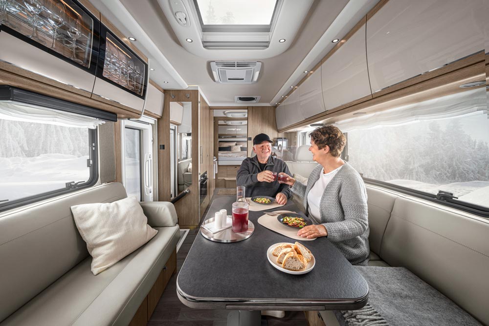 Ein älteres Paar sitzt lächelnd in einem modernen Wohnmobil und genießt ein Mittagessen