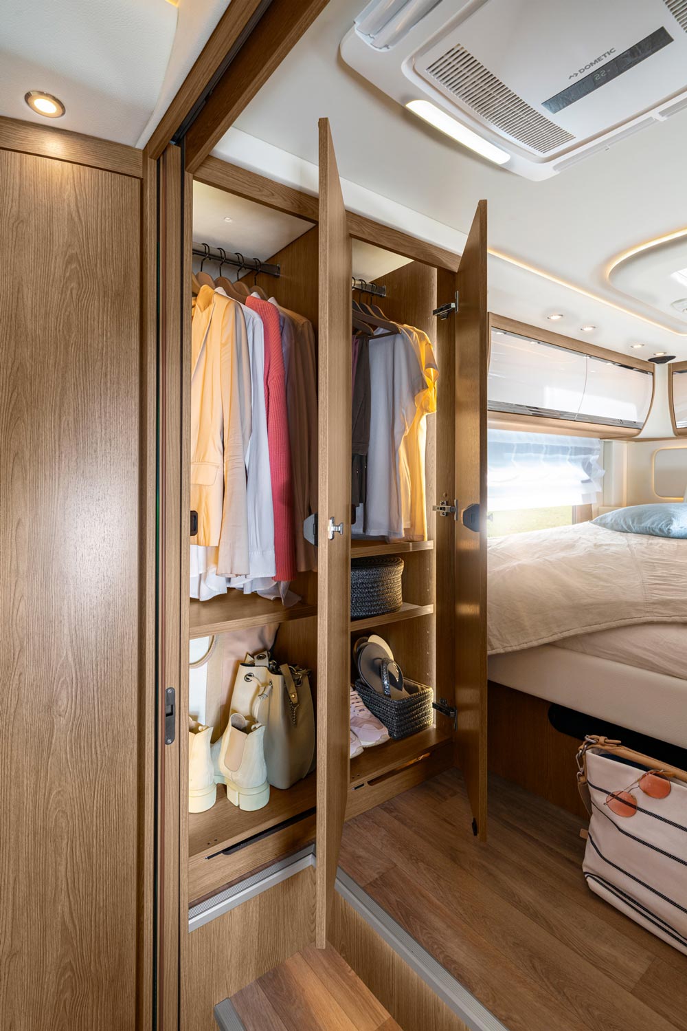 Offener Kleiderschrank in einem Wohnmobil mit hellen Kleidungsstücken und Accessoires