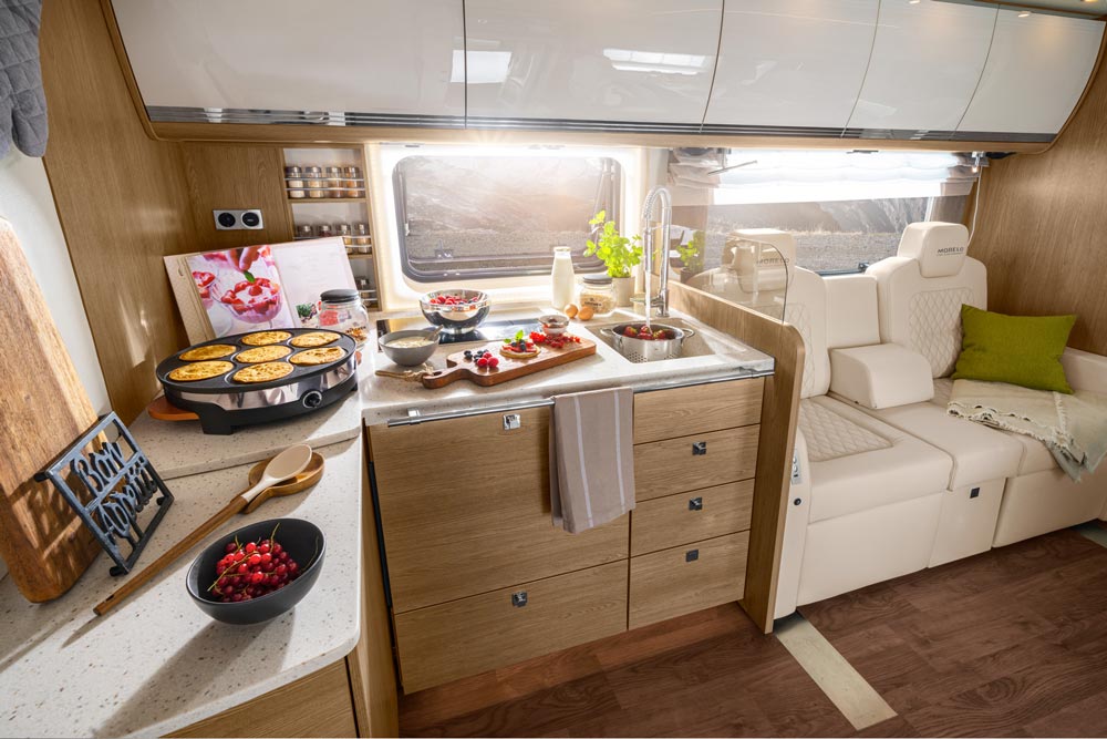 Moderne Wohnmobilküche mit hellem Holzdekor, frischen Zutaten und sonnenlichtdurchflutet