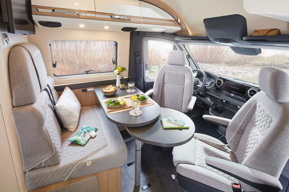 Helles Wohnmobil mit gedecktem Tisch, grauen Polstern und großen Fenstern