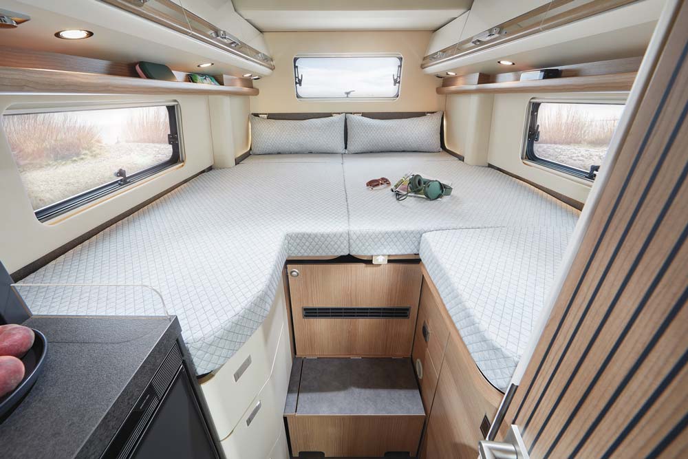 Großes gemütliches Bett in einem Wohnmobil mit hellen Holzakzenten und Fenstern