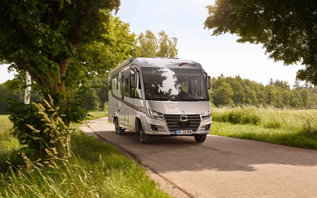 Ein silbernes Wohnmobil fährt fröhlich auf einer schmalen Landstraße im Grünen