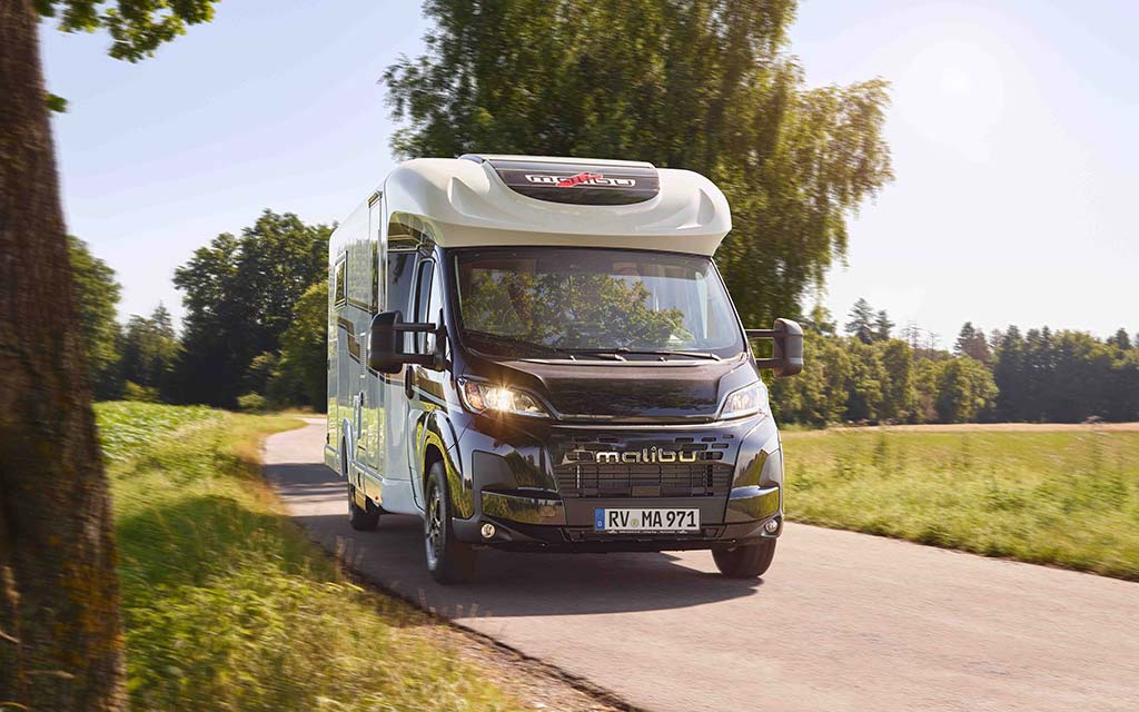 Ein schwarzer Malibu Wohnwagen fährt auf einer sonnigen Landstraße entlang