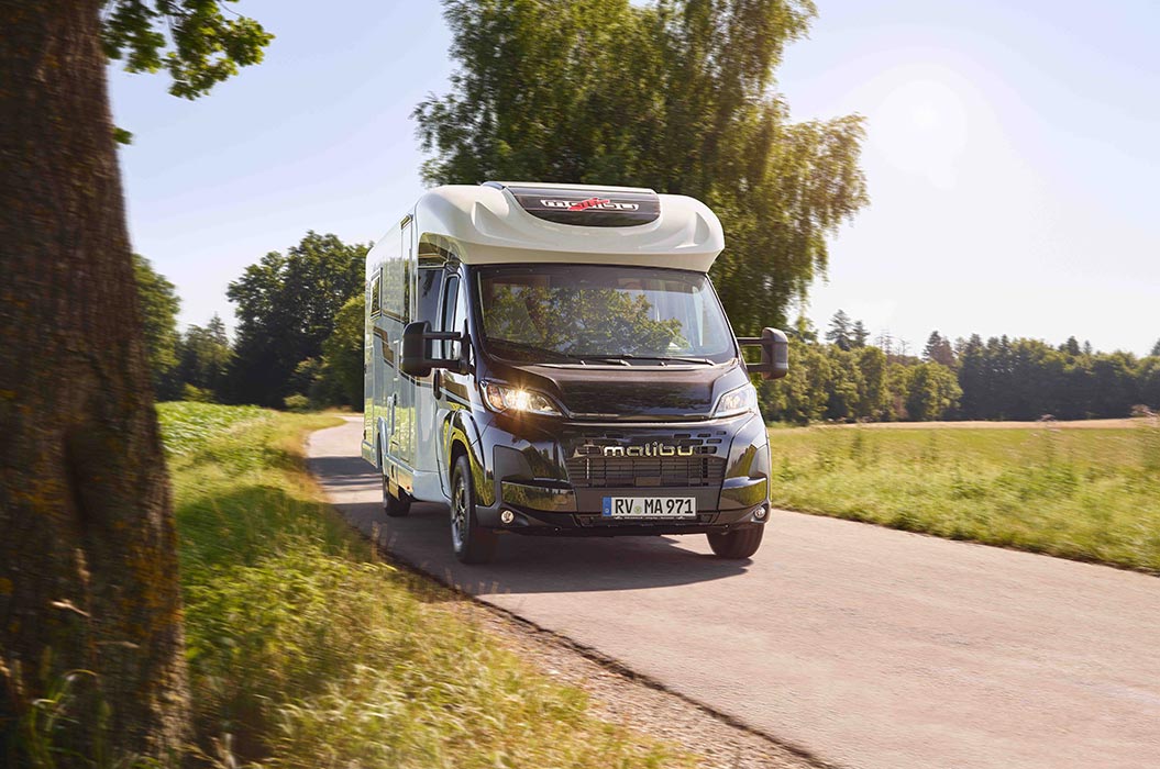 Ein schwarzes Wohnmobil mit silbernen Akzenten fährt über eine sonnige Landstraße