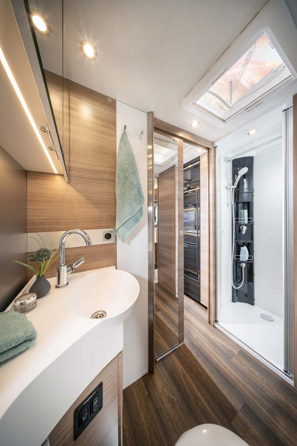 Ein modernes Wohnmobilbad mit Holzoptik, Dusche, Waschbecken und Handtuch in Grün