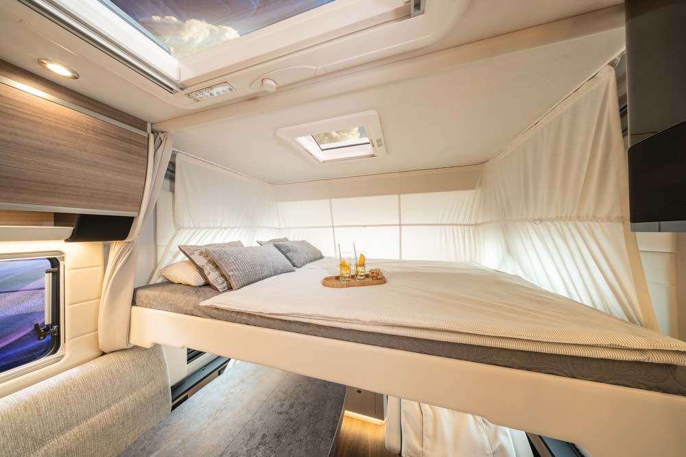 Ein gemütliches Wohnmobilbett mit hellen Kissen und Schalen mit Getränken darauf
