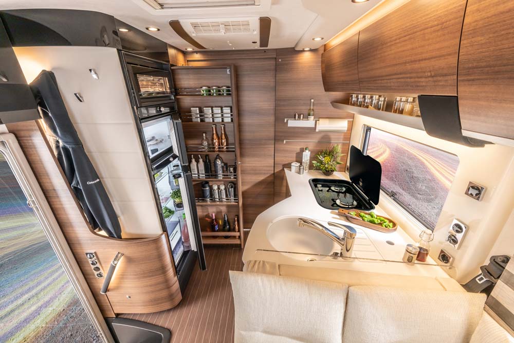 Modern Wohnmobilküche mit Holzdekor, hellem Sofa und gepflegtem Vorratsschrank