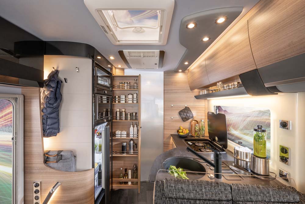 Moderne Wohnmobilküche mit hellem Holz, vielen Schränken und frischem Gemüse