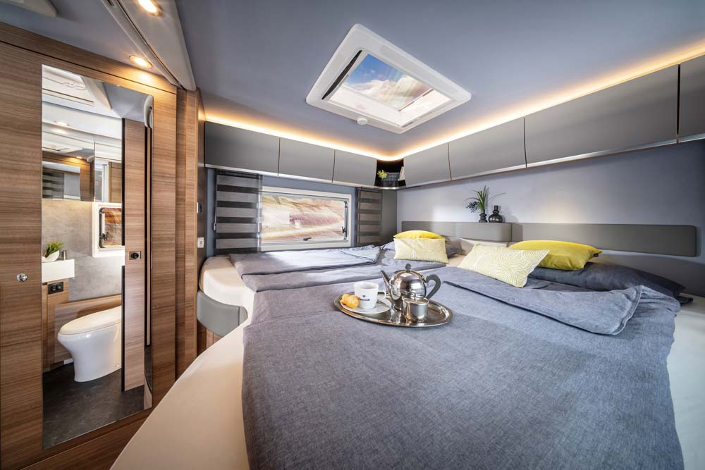 Modernes Wohnmobil Schlafzimmer mit grauer Bettwäsche, gelben Kissen und Tablett mit Tee