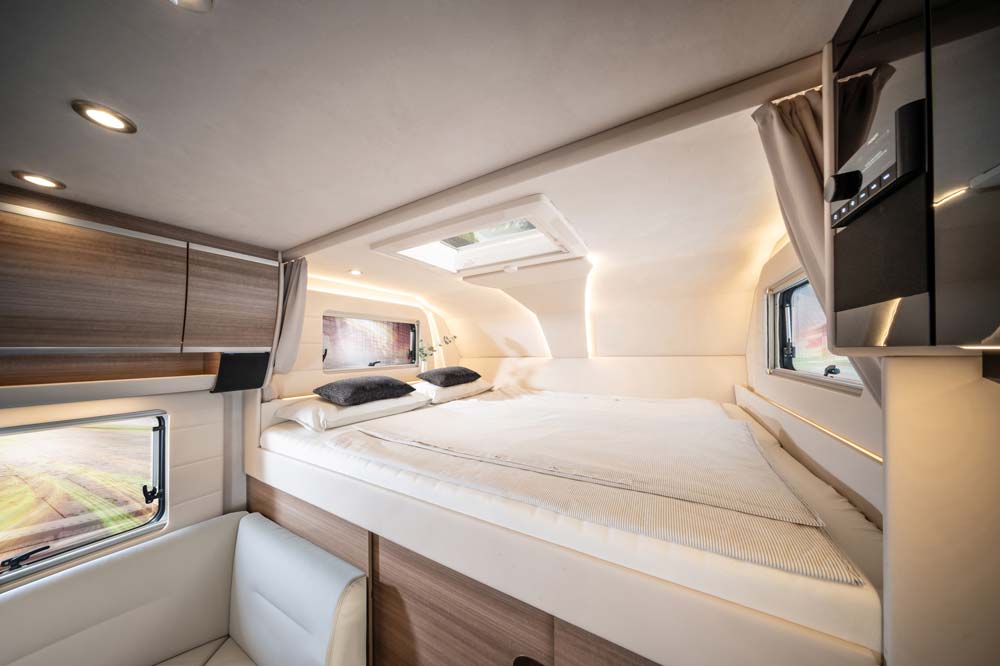 Ein modernes Wohnmobilinterieur zeigt ein gemütliches Doppelbett mit Oberlicht und stilvoller Holzverkleidung