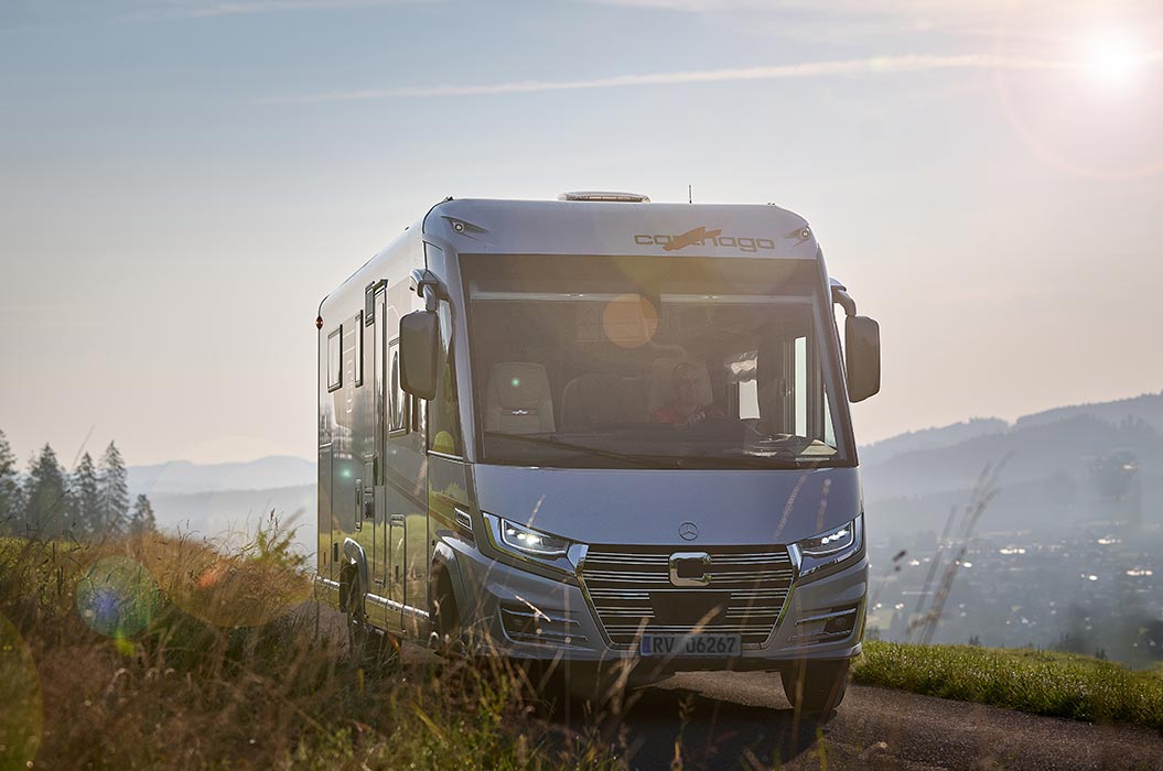 Ein silbernes Wohnmobil fährt am Morgen durch eine grüne Hügellandschaft