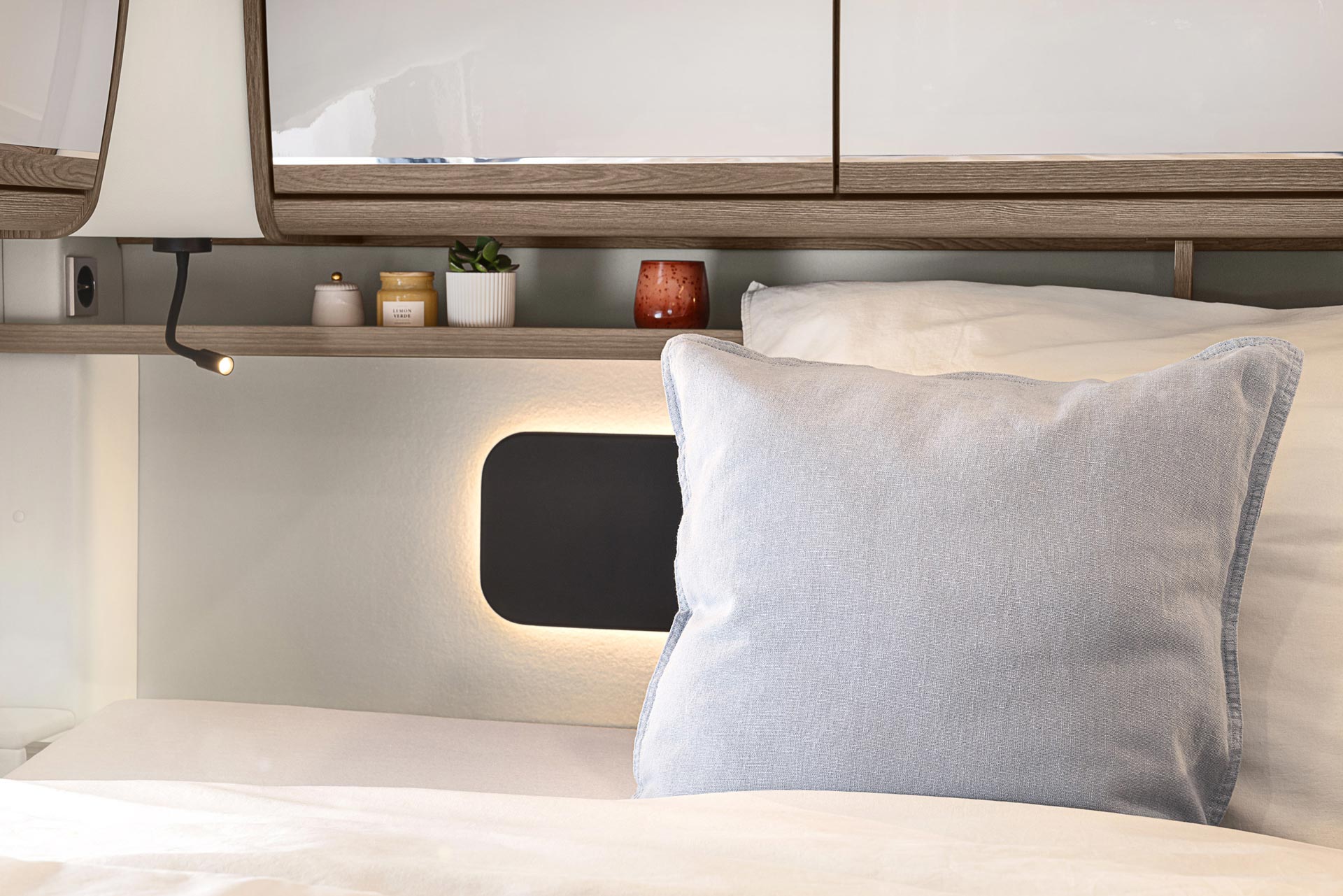 Ein helles Schlafzimmer mit einem großen hellblauen Kissen und kleinen Dekoartikeln