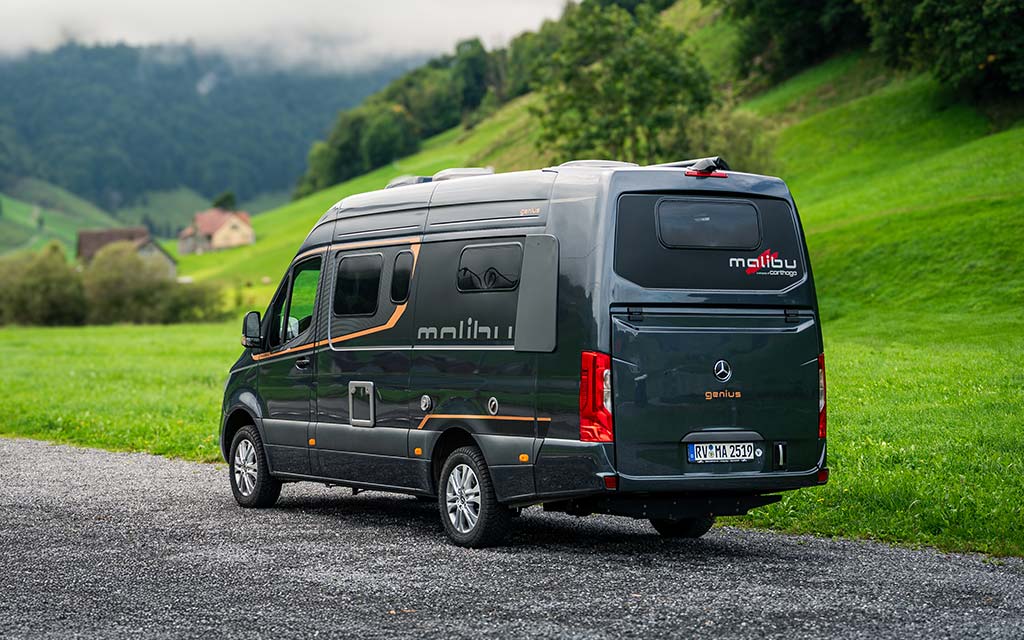 Grauer Malibu Van parkt auf einer Wiese vor Hügeln und grüner Landschaft
