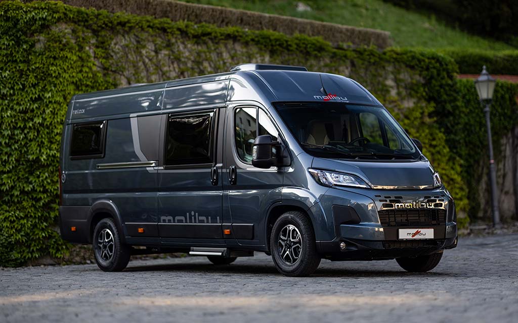 Ein silberner Malibu Wohnmobilvan steht auf Kopfsteinpflaster vor einer grünen Mauer