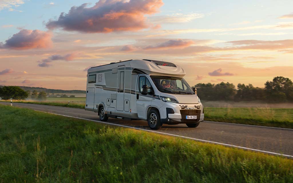 Ein weißes Wohnmobil fährt bei Sonnenuntergang durch eine ländliche Landschaft