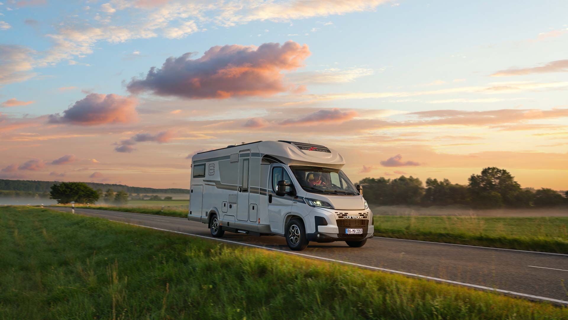 Ein weißes Wohnmobil fährt bei Sonnenuntergang eine Landstraße entlang