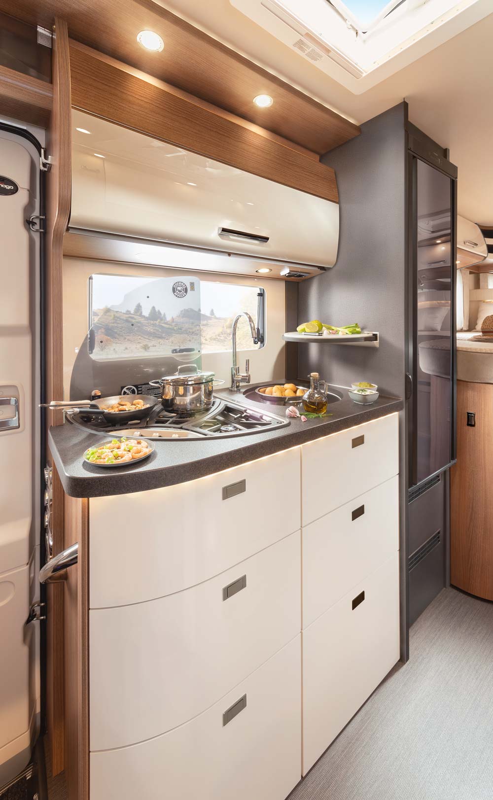 Moderne Wohnmobilküche mit Herd, frischen Zutaten und viel Tageslicht