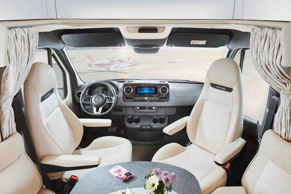 Das Cockpit eines hellen Wohnmobils mit beigen Sitzen und Blick auf Flugzeuge