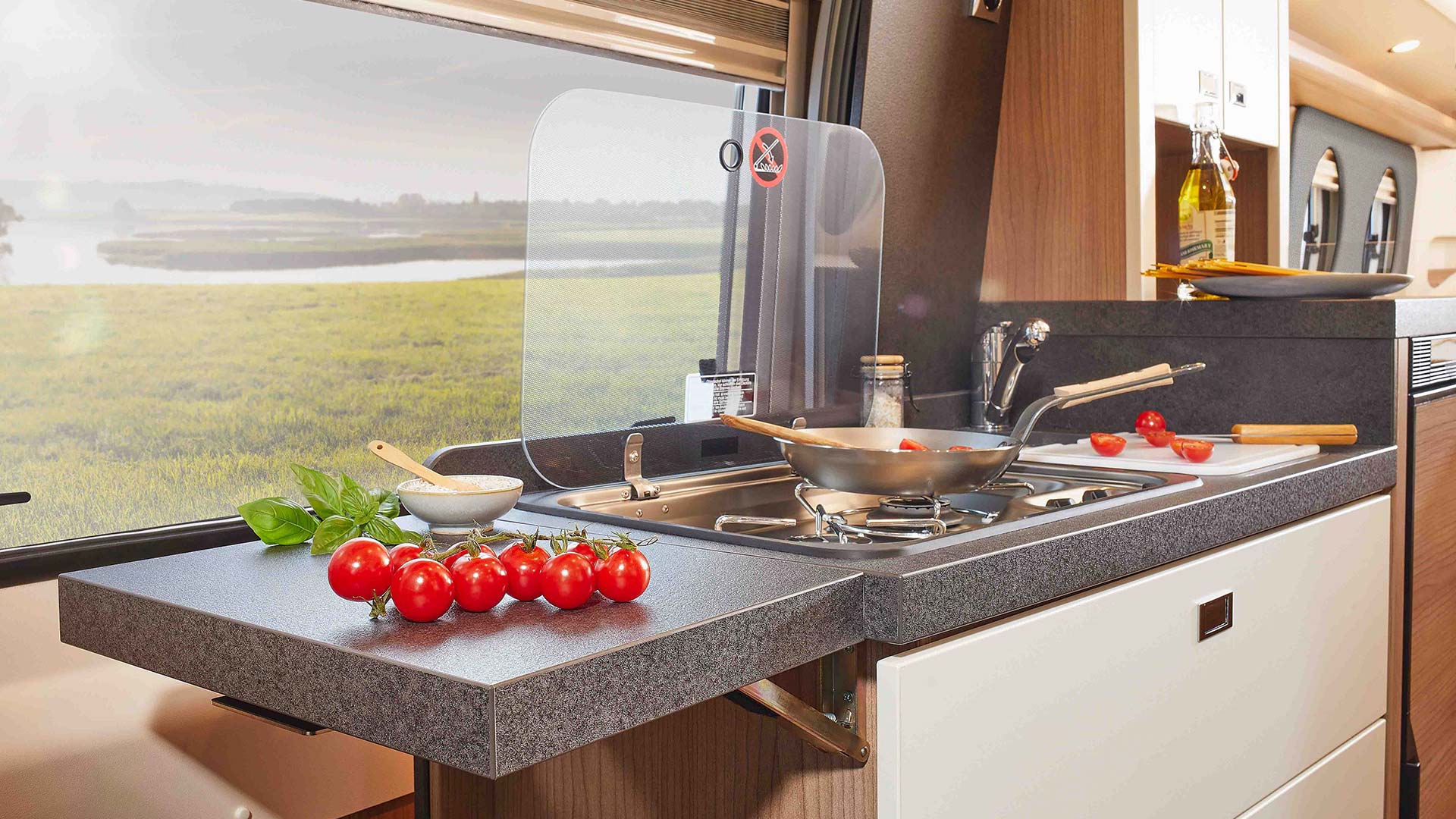 In einer modernen Wohnmobilküche liegen frische Tomaten und Kräuter auf einer grauen Arbeitsplatte