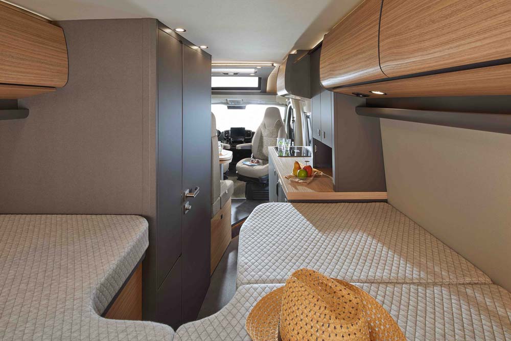 Im modernen Wohnmobil mit hellen Holzelementen liegt ein Strohhut auf dem Bett