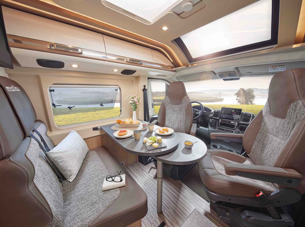 Gemütlicher Wohnmobil-Innenraum mit gedecktem Tisch, Panoramafenster und hellem Tageslicht