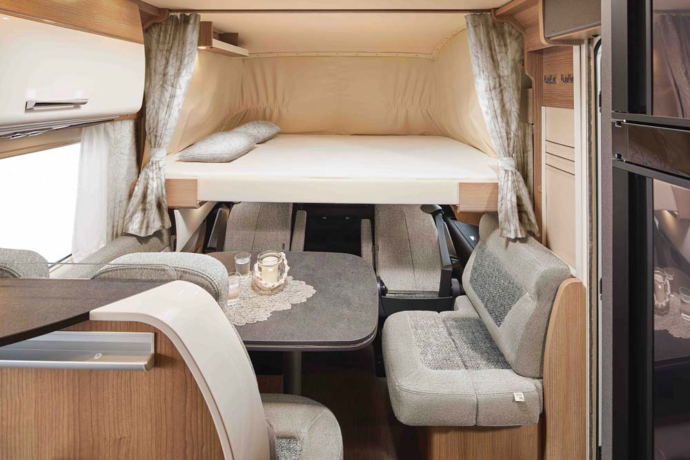 Ein gemütlicher Wohnwagen mit hellem Hochbett, grauen Sitzpolstern und gedecktem Tisch