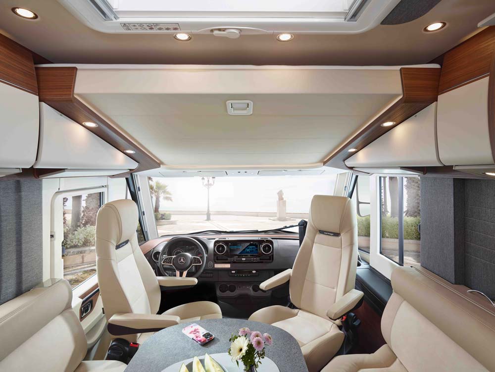 Helles Wohnmobil Cockpit mit beigen Ledersitzen und einem runden Tisch mit Blumen