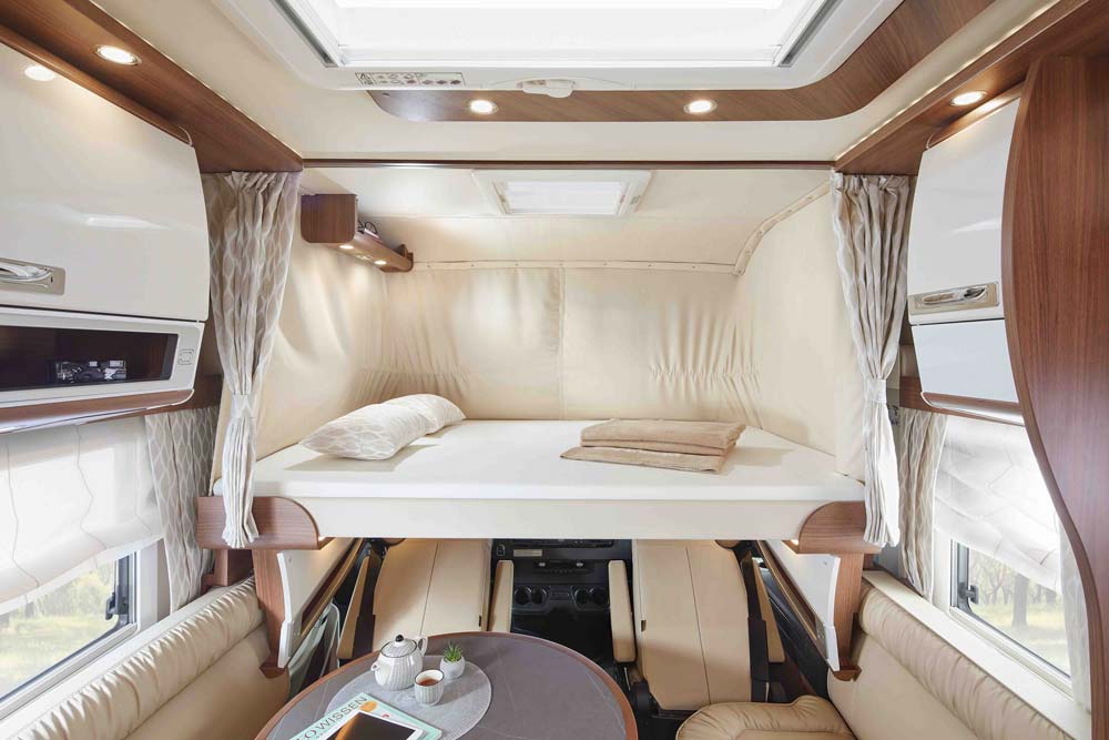 Modern und heller Wohnbereich im Wohnmobil mit hochgeklapptem Doppelbett und edlem Holzdekor