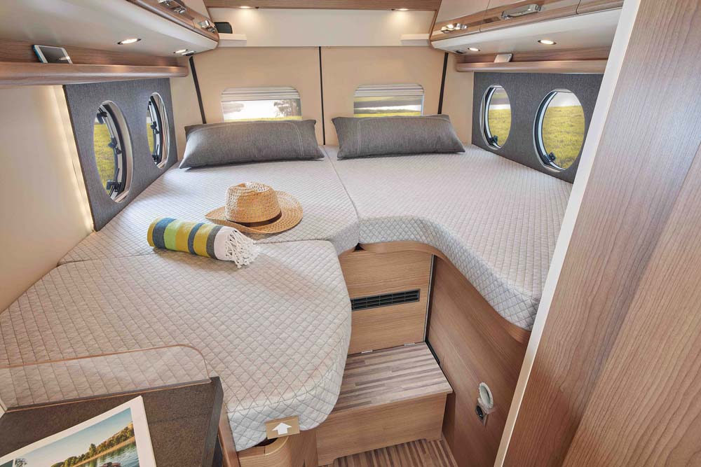 Zwei Einzelbetten mit grauer Tagesdecke und Kissen in einem hellen Wohnmobilinterieur