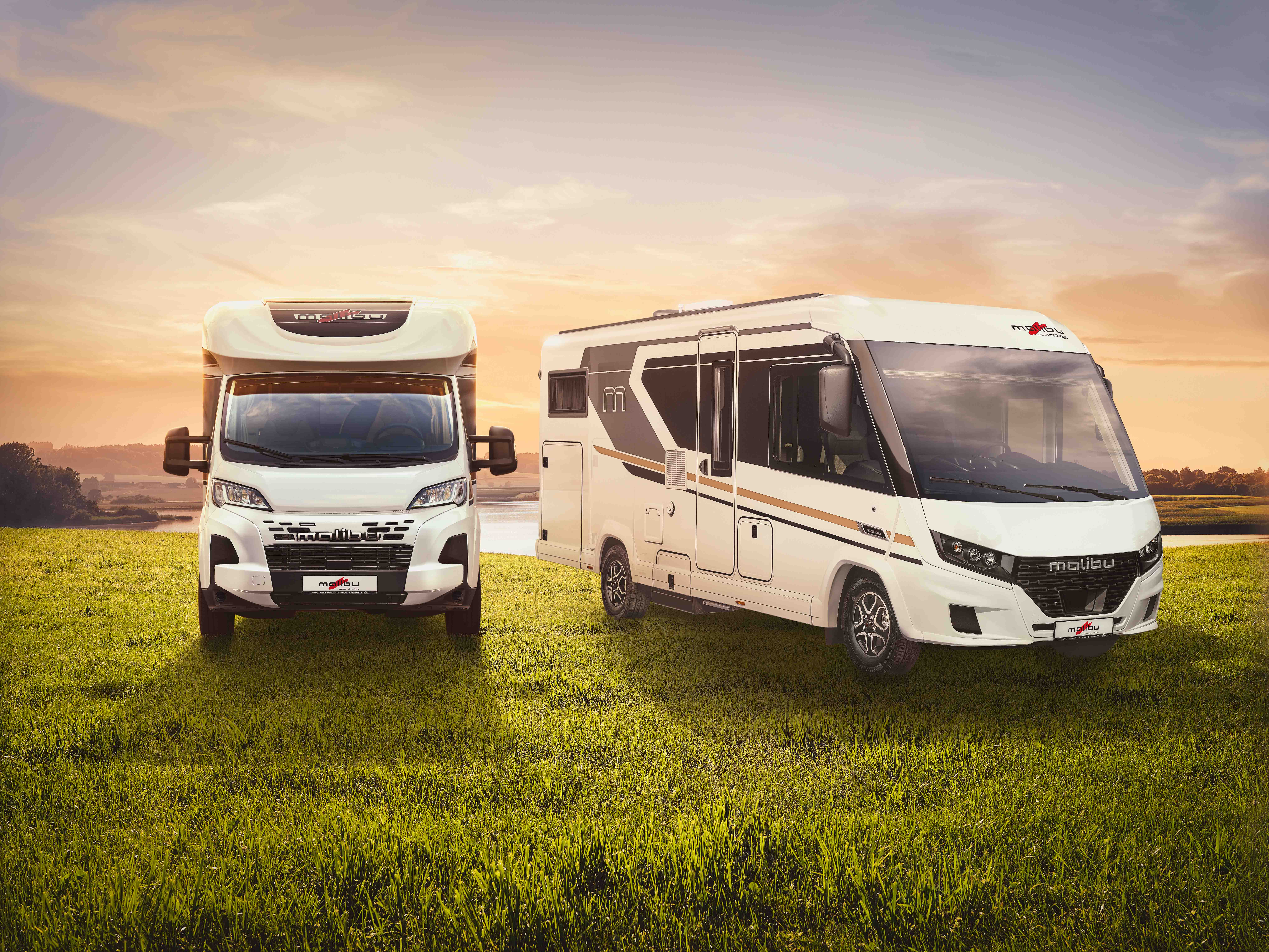 Zwei moderne weiße Wohnmobile stehen auf einer grünen Wiese bei Sonnenuntergang