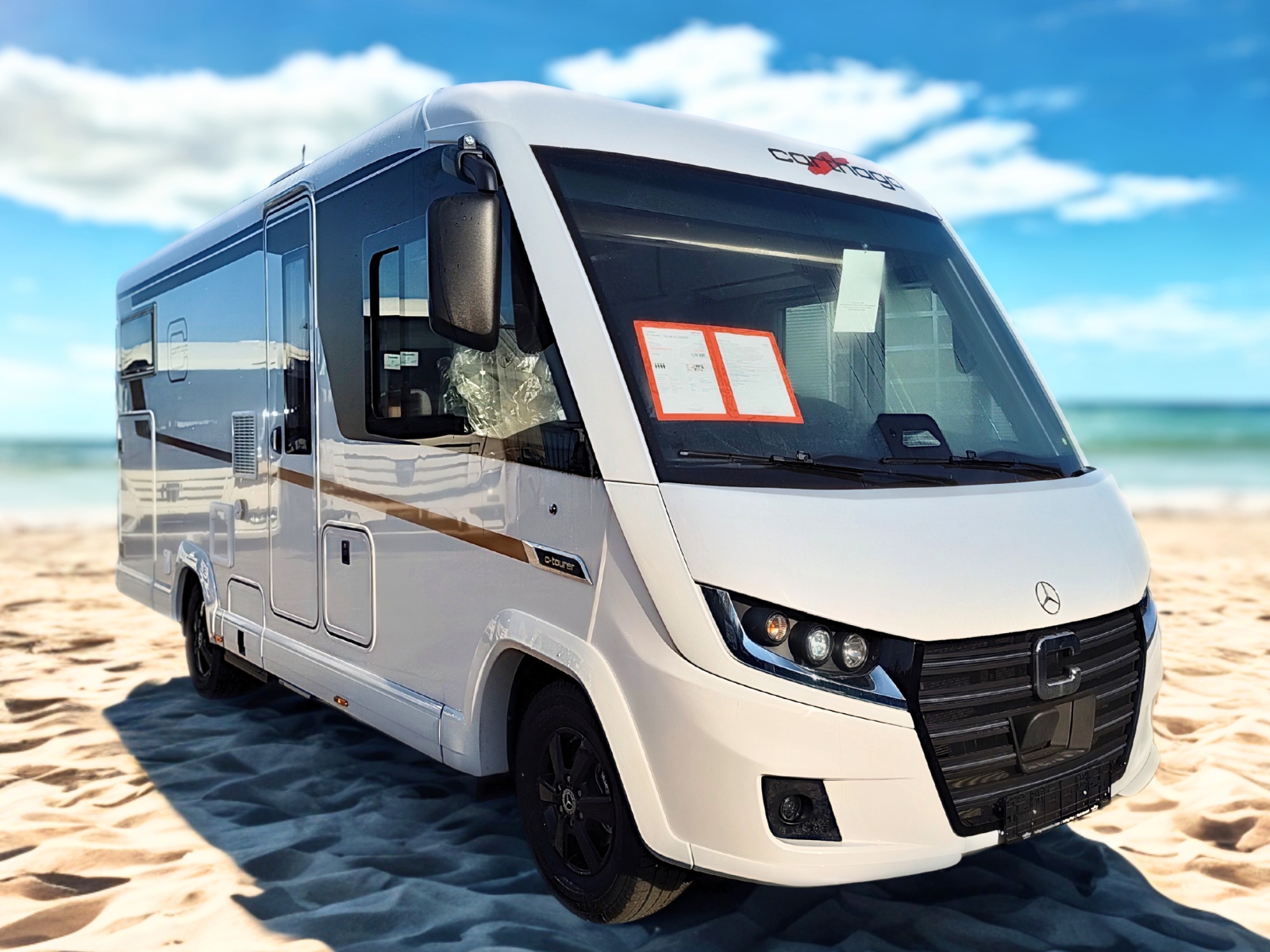 Weißer Wohnmobil auf sandigem Strand mit Sonnenlicht und schwarzem Felgendesign