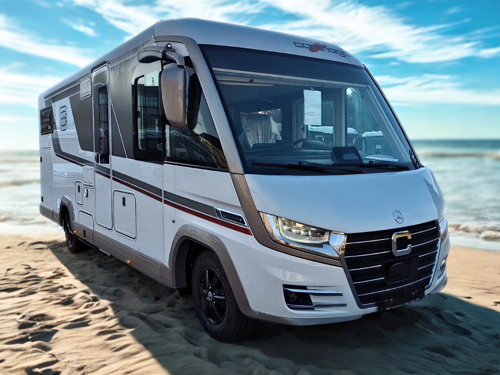 Ein moderner weißer Wohnmobilbus steht am Strand unter blauem Himmel